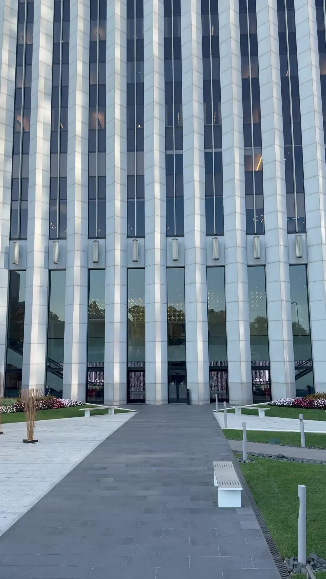 Office tower entrance, camera tilting up the white marble facade against a clear sky